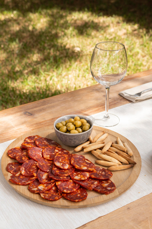 chorizo sliced on wooden plate with breadsticks and olives on an outdoor table